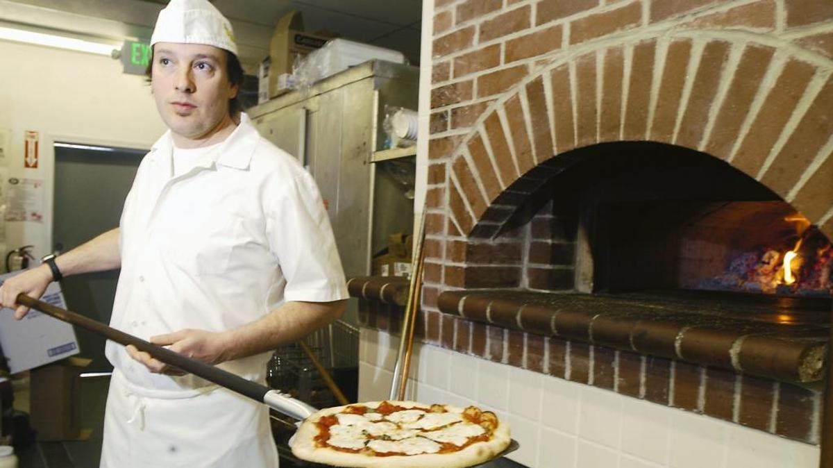 In this 2006 photo, Dan Guild pulls a pie out of Casanova Pizzeria’s wood-fired brick oven.