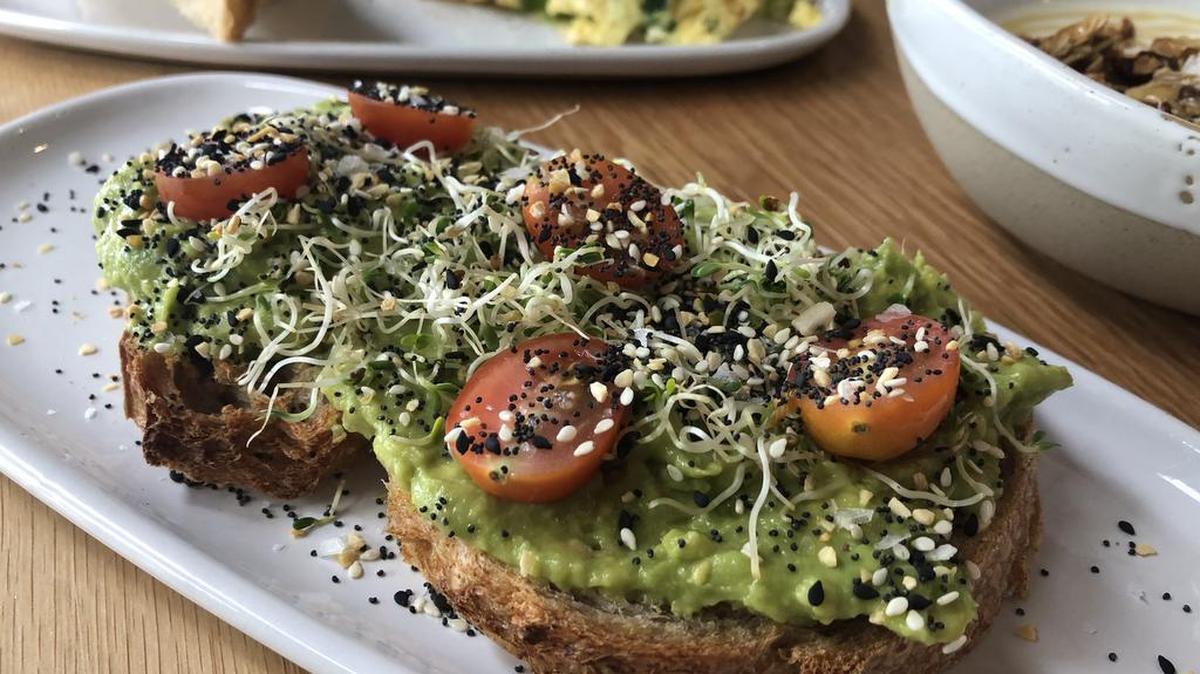 The avocado toast at ā café is topped with sliced cherry tomatoes, alfalfa sprouts and seasoning.