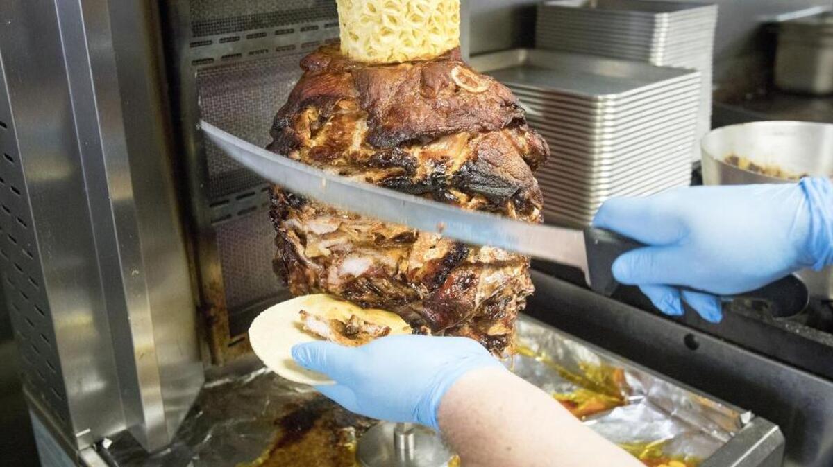 Chef Tito De la Garza carves a trompo spool of pork layered with local bacon, onion, cilantro, lime and pineapple for street tacos at Calle 75.
