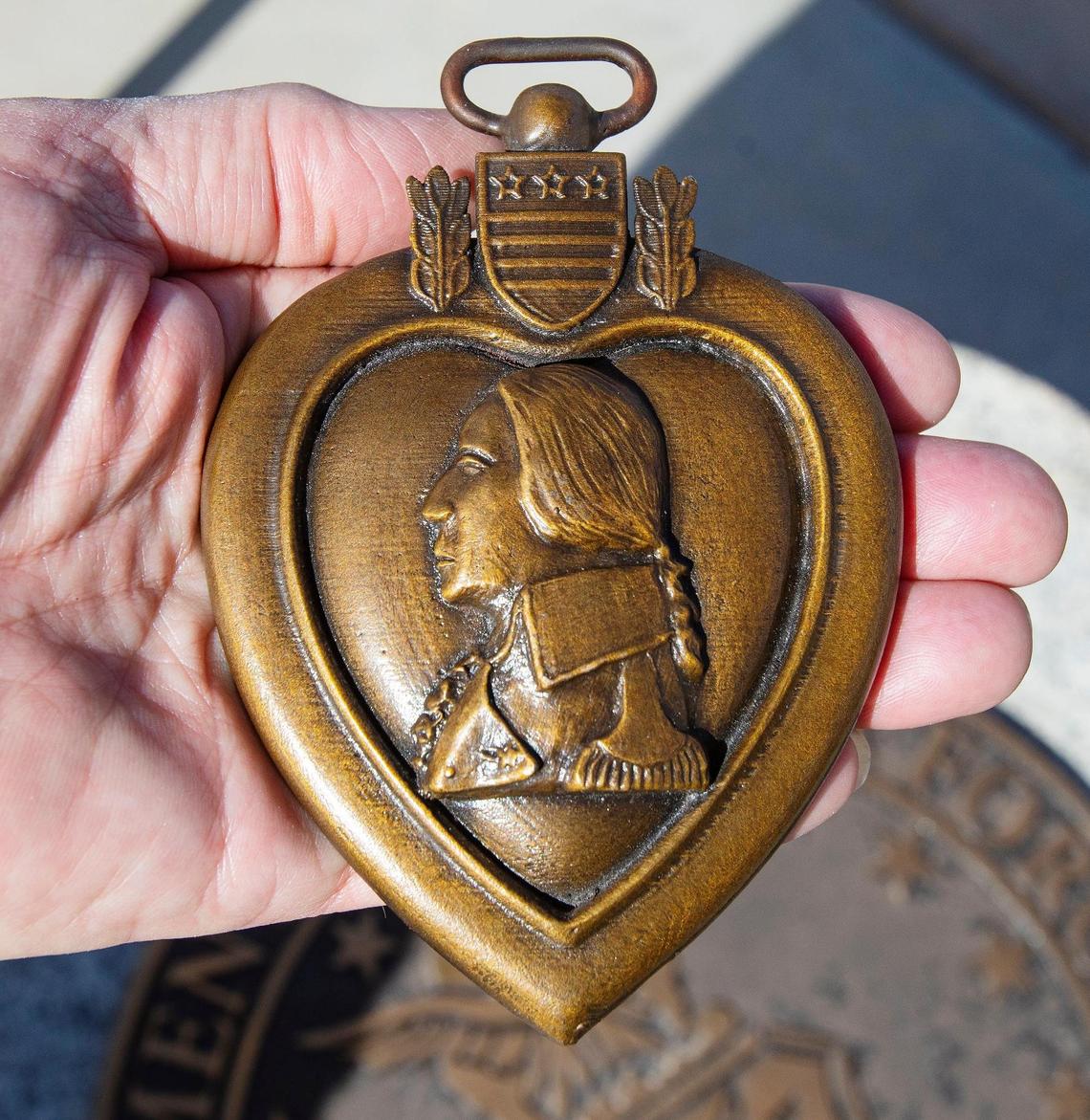 Former Idaho Governor Dirk Kempthorne holds a bronze heart. Two of these bronze hearts, in the design of the Purple Heart, contain soil from conflicts ranging from Yorktown to Vietnam and Iraq, and have been placed inside each figure of the new statue at the Idaho Veterans Cemetery.