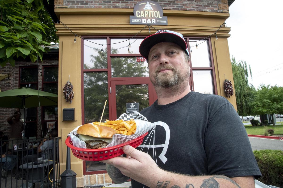 Chef Ryan Hembree holds up a Green Chile Cheesburger with spicy-seasoned fries and Distal Provisions habanero ranch sauce. Savor an order for $12 on Fridays and Saturdays at Capitol Bar on West State Street in Boise.
