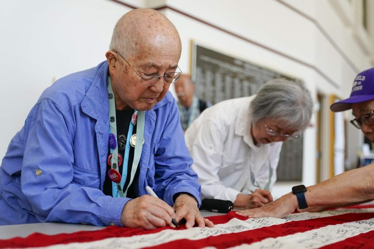 Minidoka survivor Paul Tomita, left, and wife Mabel Tomita, right, a survivor of Tule Lake and Gila River, sign a World War II-era 48-star flag as part of a project by Judge Johnny Gogo of Santa Clara County Superior Court at the College of Southern Idaho in Twin Falls. Gogo started the project to promote Fred Korematsu Day and has traveled around the country gathering signatures from survivors, filling several flags he has donated to Japanese American museums.