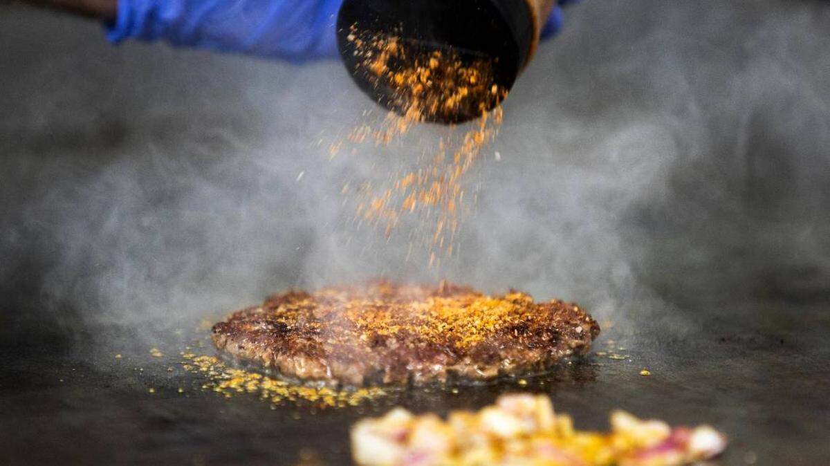 An image of a burger patty being grilled and seasoned.