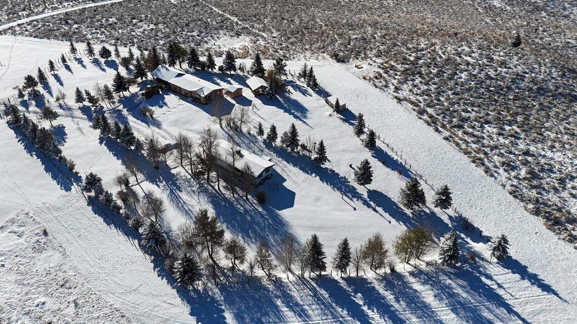 Multiple farm houses on the property sit behind a row of trees.