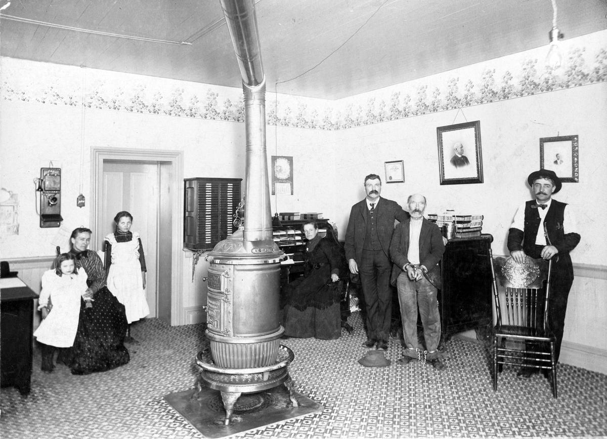 James Hogan is in custody in 1901 at the Ada County Sheriff's office in the Ada County Courthouse. From left: Alberta Rebecca Daly, Mrs. Rebecca Daly, Zelma Lee Daly. Right of the stove pipe: (unknown woman), Sheriff Joe Daly, "Hogan the Stiff," Deputy Andy Robinson.