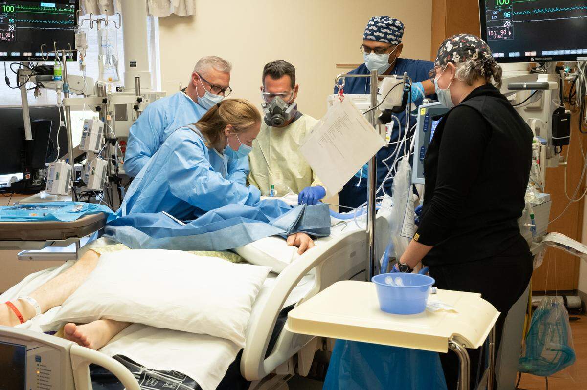 Health care workers in the ICU at Saint Alphonsus Regional Medical Center operate on a patient afflicted with COVID-19. This patient had been intubated with a breathing tube for two weeks, but continued to deteriorate. They have removed the endotracheal tube and are opening the trachea to insert a more permanent tube, a procedure called tracheostomy.