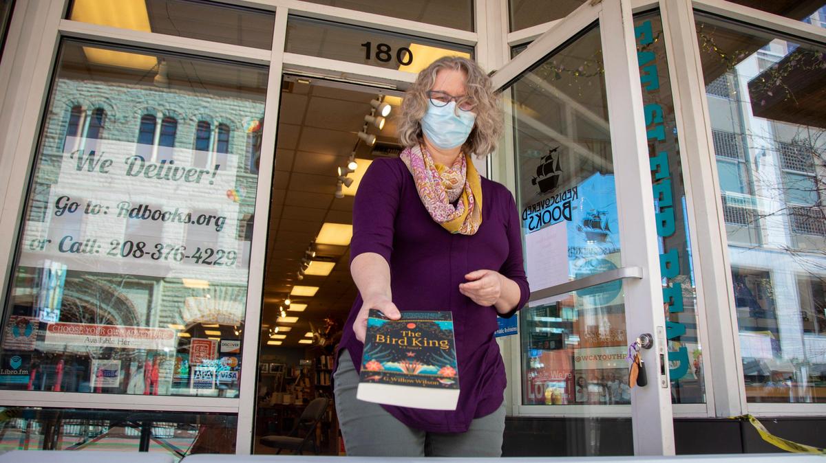 Laura DeLaney, co-owner of Rediscovered Books, offers curbside service to customers who order books online. She places the book on a table outside the store when the customer arrives. The store will continue operating this way for the time being even though DeLaney is allowed to reopen on Saturday.