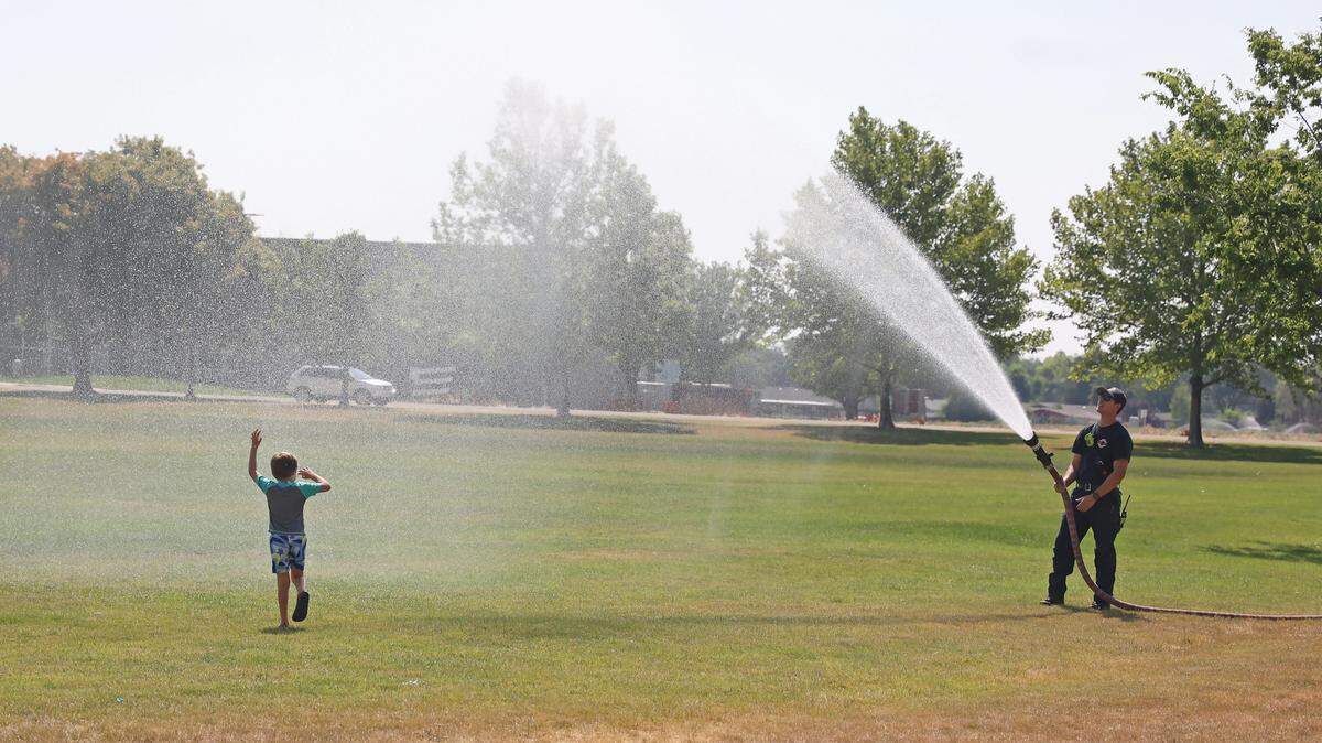 Caldwell firefighter Mike Aguilar sprays water into the air as Oliver Shetler, 6, runs by, at Brothers Park in Caldwell, Wednesday, July 10, 2024. 