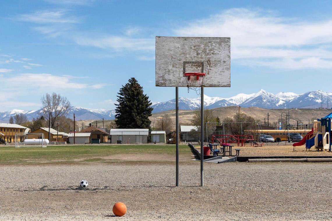 An old basketball hoop stands in front of newer playground equipment on the backside of the elementary school in Salmon.