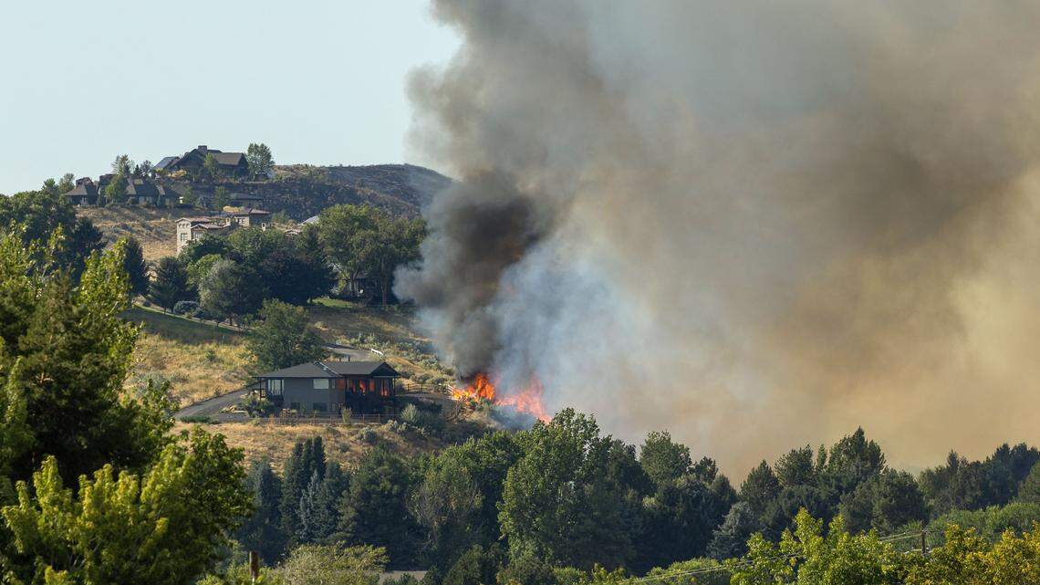 Firefighters battle to save a home as wind-driven flames climb a hillside north of Beacon Light Road, Monday, Aug. 18, 2025.