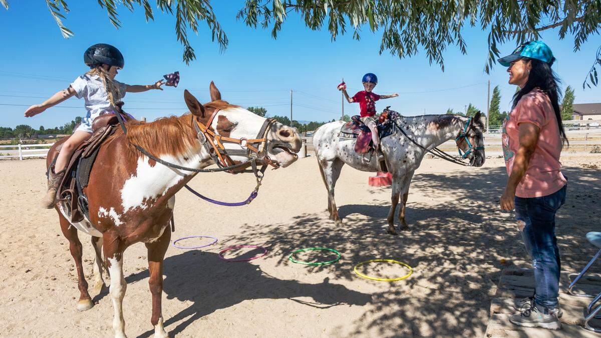Siblings Jemma Fratti, 7, and Porter&nbsp;Fratti, 9, throw bean bags&nbsp;into hula hoops on horseback as a balance drill on with horses Tess and Maverick and instructor Katie Blessinger during an evening lesson at Brookside Horses in Kuna, Tuesday, July 18, 2023. As temperatures rose into the 90s, many of the lesson drills were held under the shade of a large tree.