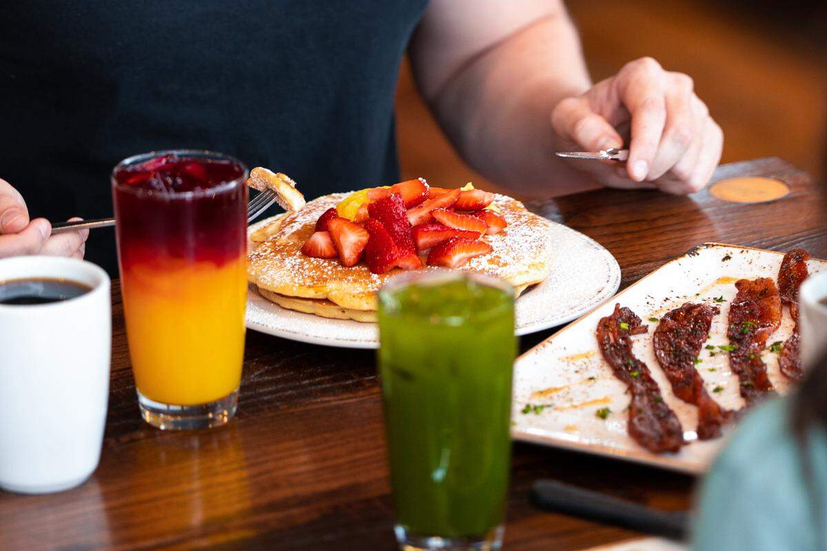 In addition to plates of pancakes and sides of Million Dollar Bacon (hardwood smoked bacon glazed with brown sugar, black pepper, cayenne and a maple syrup drizzle), diners can expect drinks such as the Kale Tonic, foreground (kale, Fuji apple, English cucumber and lemon) and colorful Morning Meditation (orange, lemon, turmeric, organic ginger, agave nectar and beet).