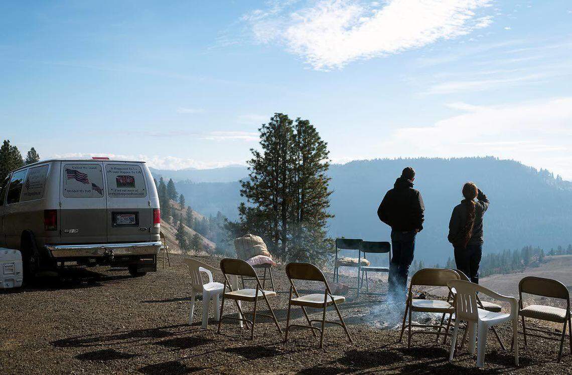 Nickerson family supporters stand alongside a smoldering fire from the previous evening as they look over their former property on Crow Bench Road east of Orofino on Wednesday afternoon.