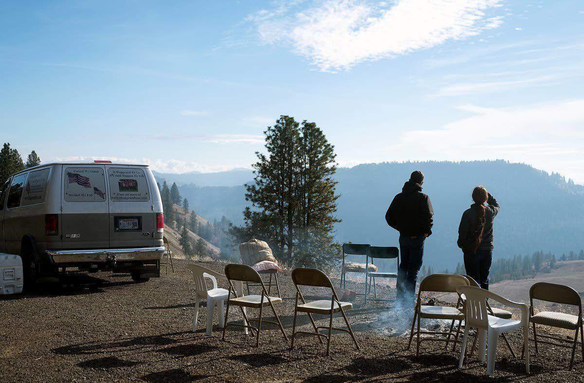 Nickerson family supporters stand alongside a smoldering fire from the previous evening as they look over their former property on Crow Bench Road east of Orofino on Wednesday afternoon.