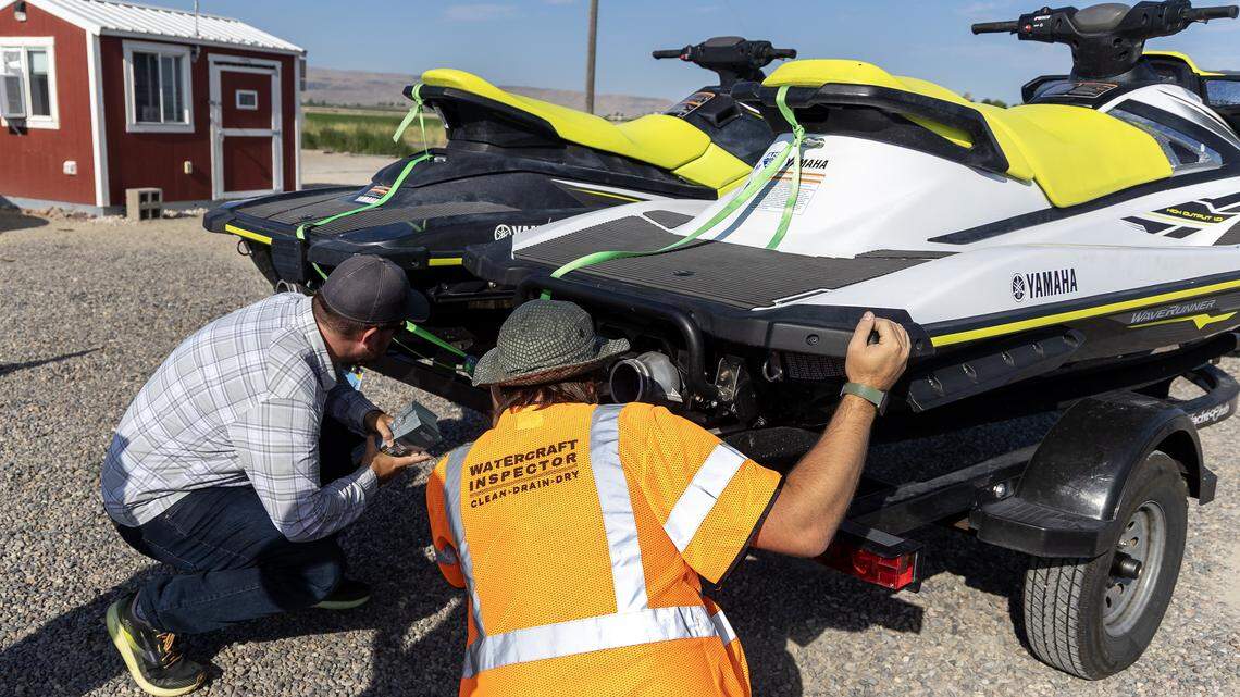 Watercraft inspector Mark Klug, right, looks at drain plugs on two jet skis last used in Nevada at a watercraft boat inspection station in Marsing, Friday, July 25, 2025.