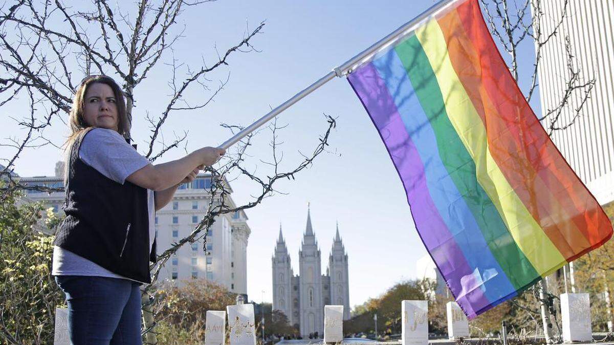 FILE - In this Nov. 14, 2015, file photo, Sandy Newcomb poses for a photograph with a rainbow flag as Latter-day Saints gather for a mass resignation from The Church of Jesus Christ of Latter-day Saints in Salt Lake City. LDS leaders tell gay and lesbian church members that attraction to people of the same sex is not a sin or a measure of their faithfulness. But they remind those members that acting on those feelings by having sex violates fundamental doctrinal beliefs that won’t change. The message is part of the Mormon church’s “Mormon and Gay” website launched Tuesday, Oct. 25, 2016, with dozens of articles, teachings, videos and stories from Latter-day Saints who identify themselves as gay.