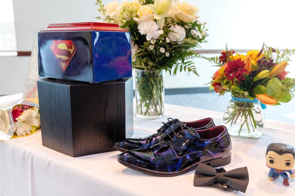A Superman-themed urn is surrounded by flowers and personal items including shoes and a bowtie of J.J. Saldaña at his memorial.