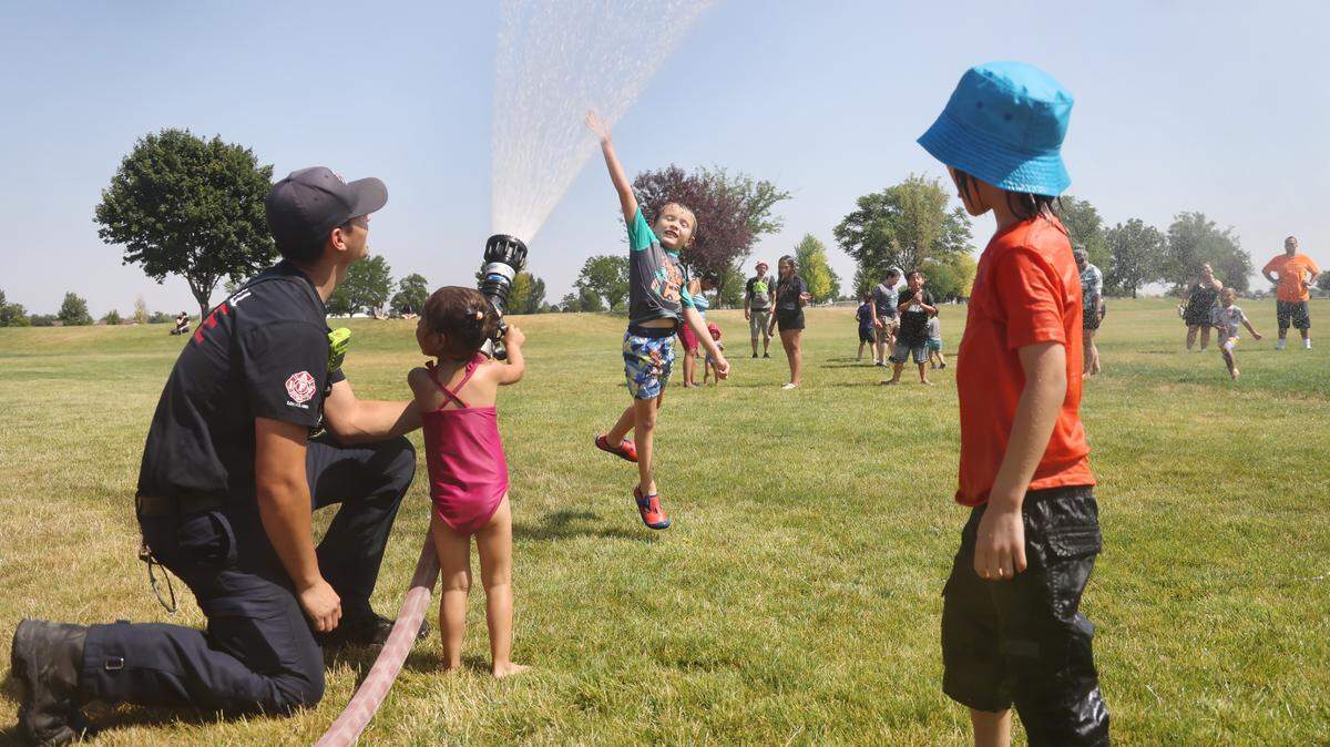 Caldwell firefighter Mike Aguilar sprays water into the air as Oliver Shetler, 6, jumps to touch the water at Brothers Park in Caldwell during 100-degree weather in this file photo from 2024. Tuesday, May 12 is expected to be as hot as 97 degrees.