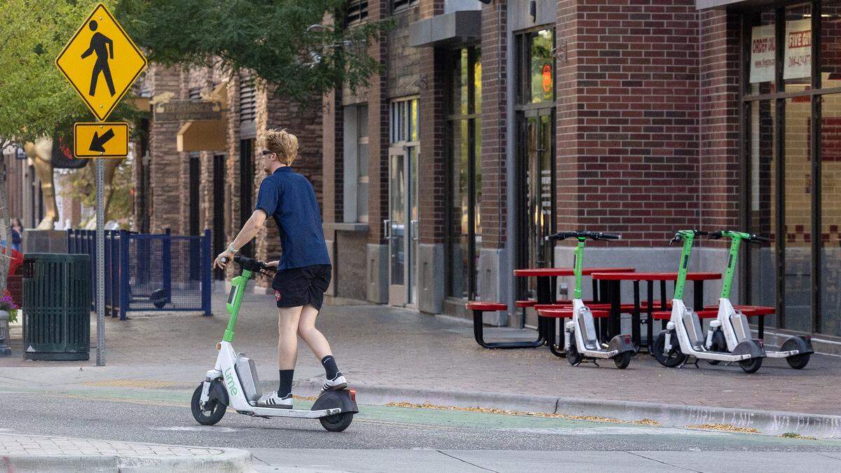 A person rides a Lime e-scooter on 8th Street in BoDo, as more scooters are parked nearby ready for use. There are more than 1,000 scooters available in the city each day.