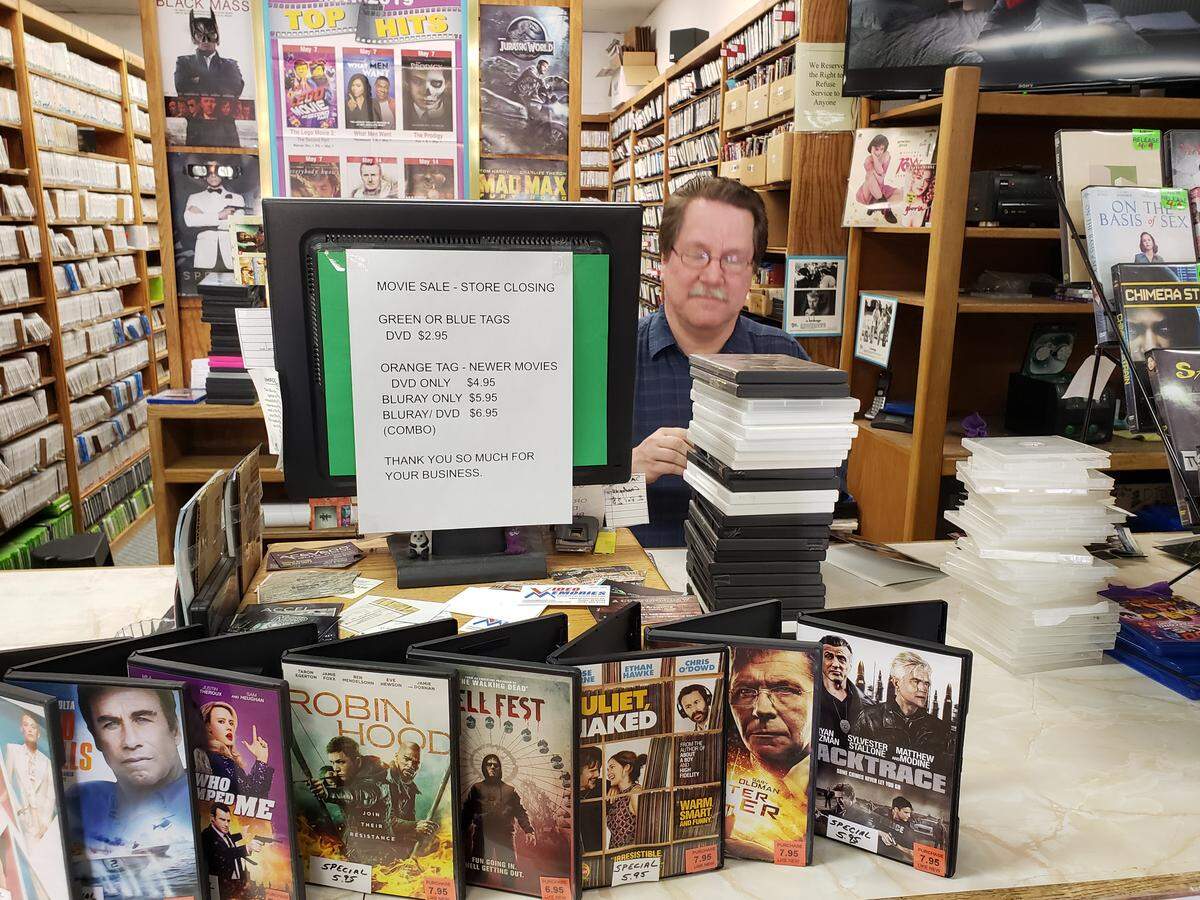 Store clerk Gerry McClure checks in movies while a sign on a computer terminal advertises movies for sale ahead of Video Memories’ June 12 closing.