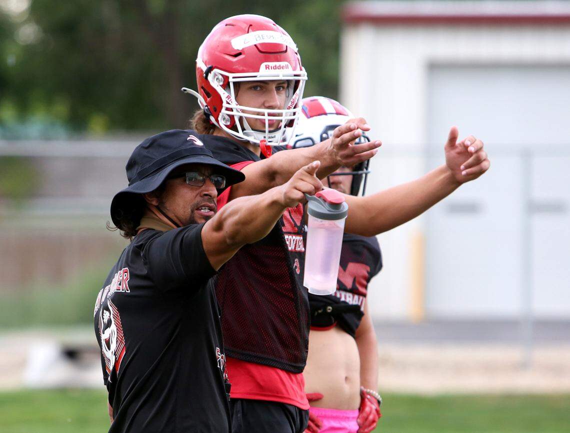 Melba coach Juan Colunga, left, and junior quarterback Cache Beus go over a play during a preseason practice Thursday at Melba High.