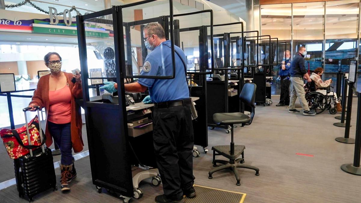 Transportation Security Administration Officer Charles Critell helps a traveler from behind a protective barrier Wednesday at the Boise Airport. To protect employees and travelers during the coronavirus pandemic, TSA has improved personal protections and installed new scanning equipment to minimize contact points.