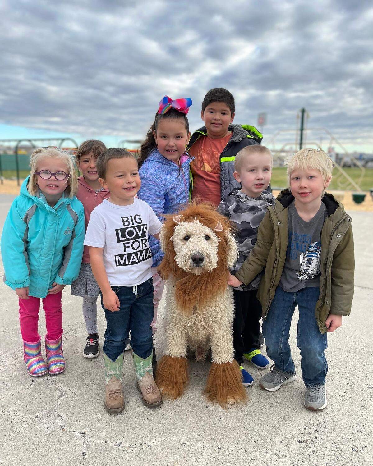 Finn is a goldendoodle at the Bliss School District. He is posing with students at the playground in his lion costume.