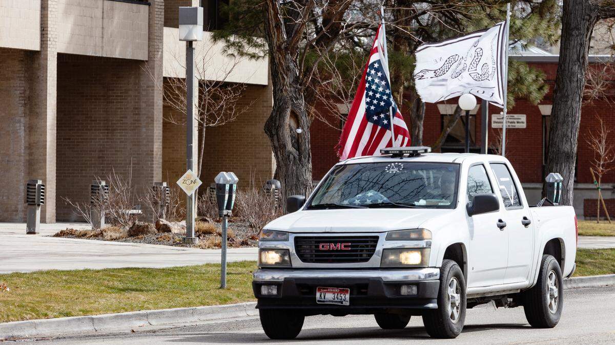 A truck with an upside-down American flag and a broken snake flag repeatedly circles a block surrounding the Idaho Department of Health and Welfare honking its horn in protest of a custody ruling that relinquished a 10-month-old Meridian child to the state.