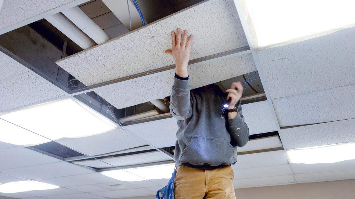 A Valley View maintenance worker removes ceiling tiles to look at a crack in a support beam above a classroom.