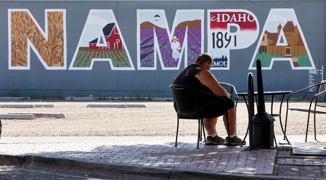 Robert Wade, a resident of downtown Nampa, sits in the shade of a tree near a mural painted on a business wall.
