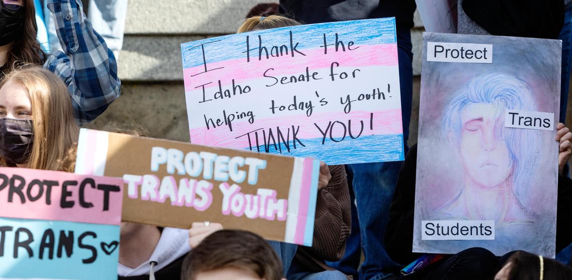 Transgender people, allies and family members of trans youth hold signs while sitting on the steps of the Idaho Capitol during a rally to celebrate the defeat of a legislative bill that would have criminalized gender-affirming health care for children.
