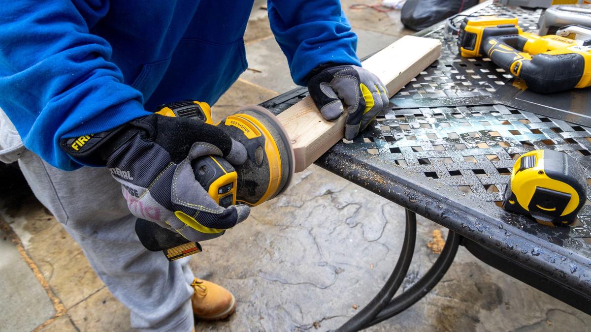 A job trainee sands a two-by-four that will fit into an Adirondack chair.