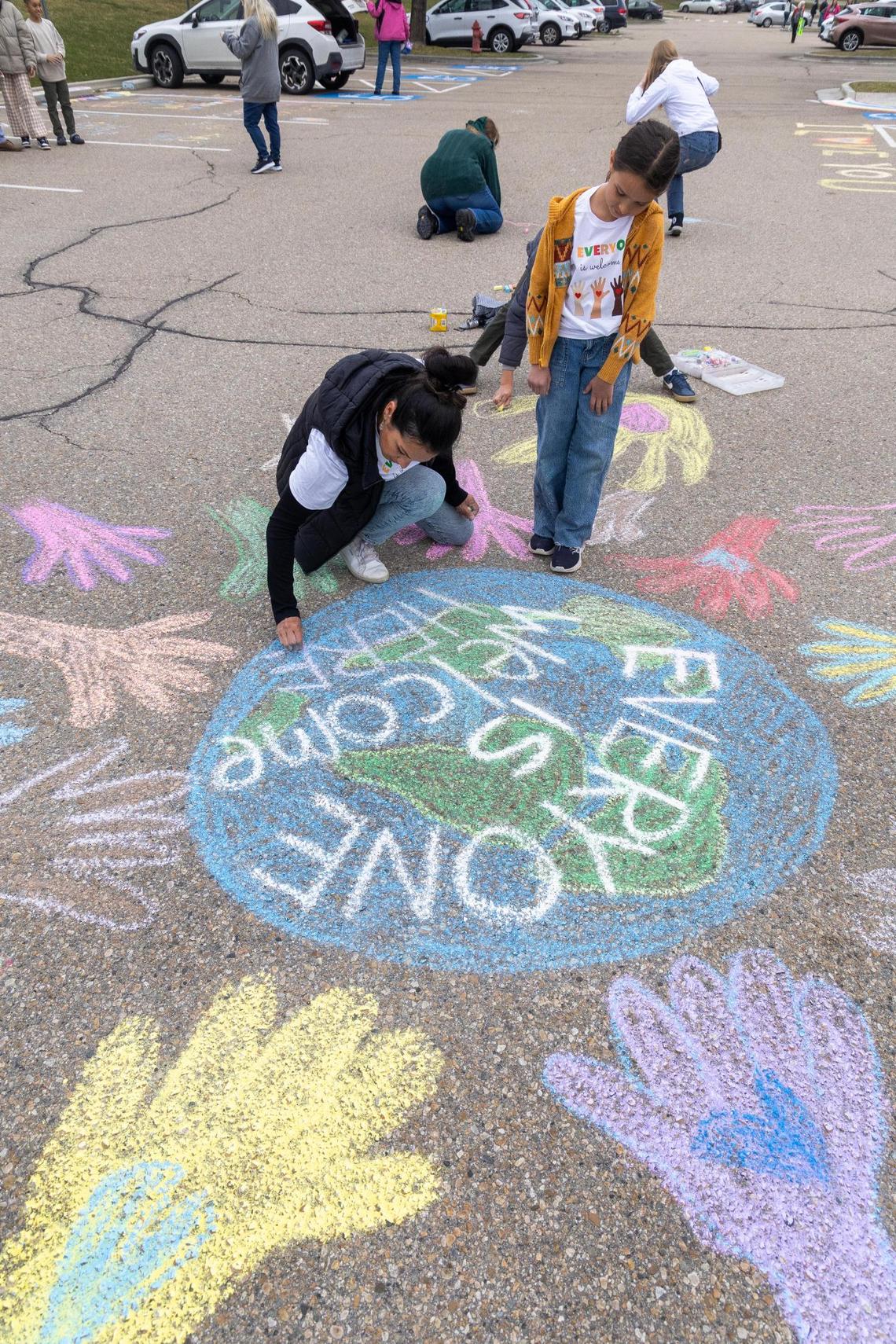 Parent Mercedes Gorham uses chalk to draw a picture of the Earth with the words “Everyone is welcome here” in the parking lot of the West Ada School District office.