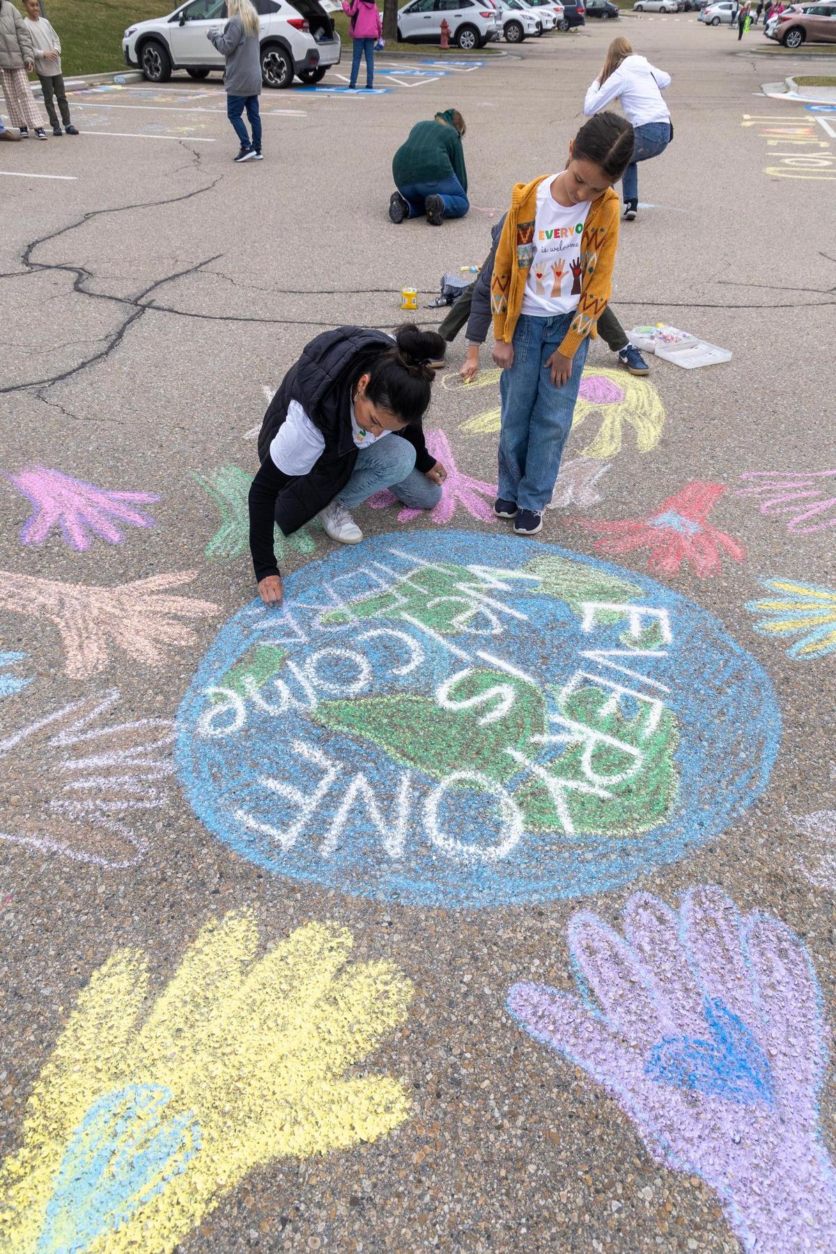 Parent Mercedes Gorham uses chalk to draw a picture of the Earth with the words “Everyone is welcome here” in the parking lot of the West Ada School District office.