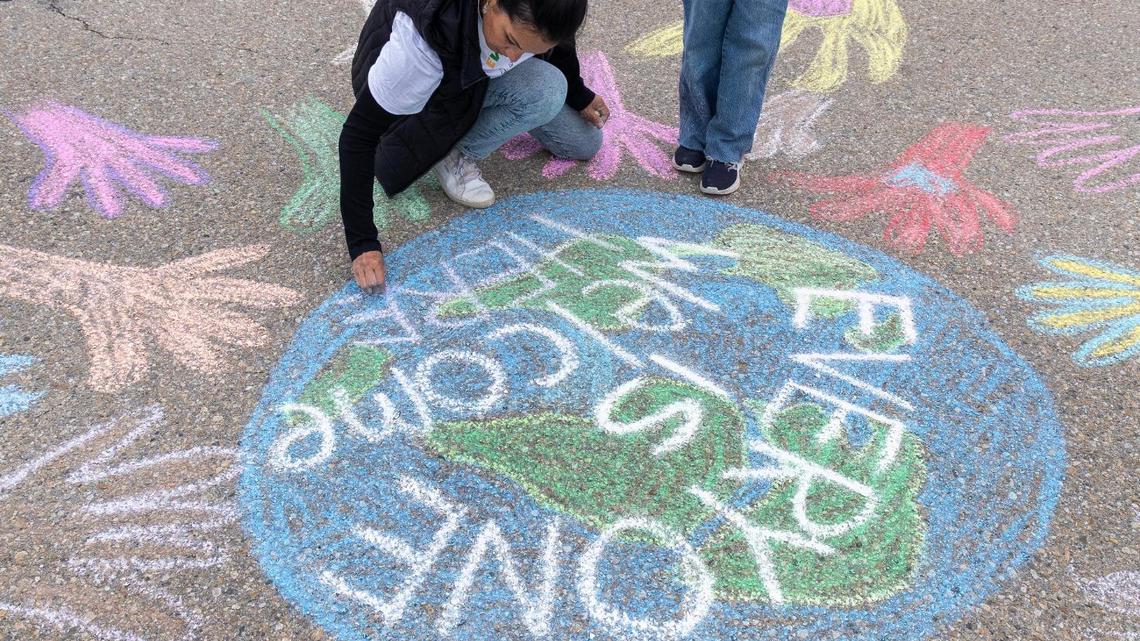 Parent Mercedes Gorham uses chalk to draw a picture of the Earth with the words “Everyone is welcome here” on Sunday in the parking lot of the West Ada School District office in Meridian. The event was a community response to the school district instructing a middle school teacher to remove a sign in her classroom that reads, “Everyone is welcome here.”