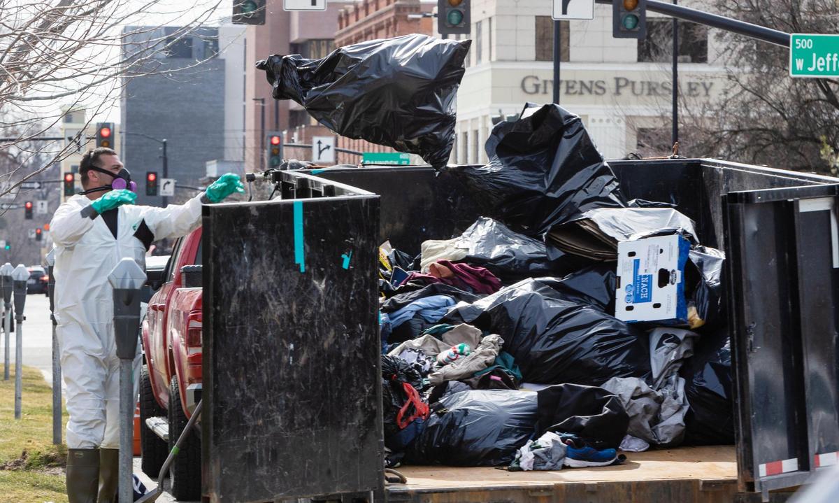 People in protective clothing throw away bags of items from the homeless protest in downtown Boise on Friday.