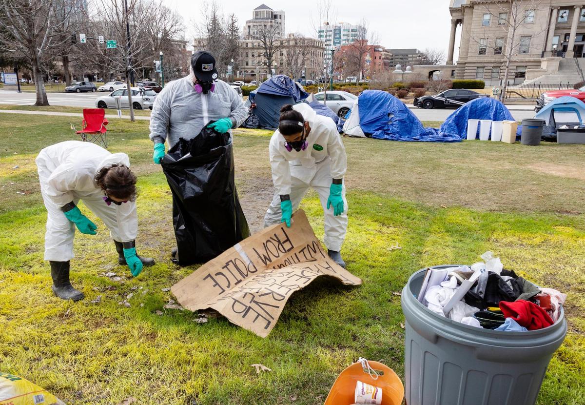 Workers in hazardous material suits pick up trash from a lawn adjacent to the Idaho Capitol after removing several tents from a protest there in March 2022.