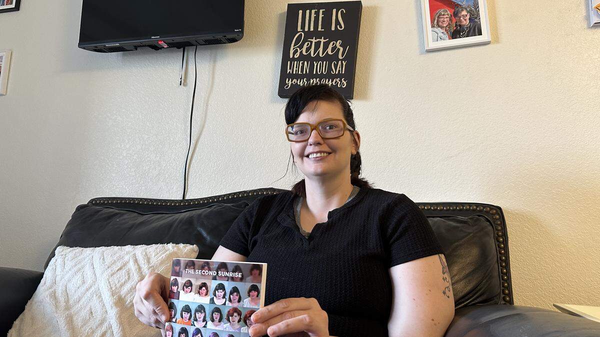 Katie Hodges holds up her book, “Bruised Not Broken,” in her Nampa apartment on Feb. 13, under a framed photo of her and her mother, Renee Hatchett.