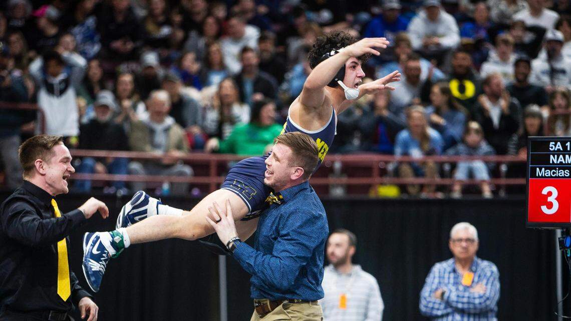 Meridian coach Brad Muri lifts Jerimiah Gonzalez after he won the 5A 113-pound state wrestling title Saturday. The Warriors also won their third straight team title.