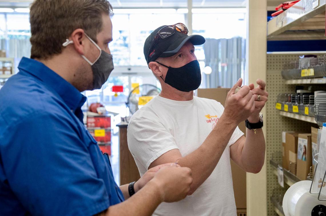 Grover’s Pay & Pack Electric and Plumbing employee Noah Thompson, left, helps customer Phil Tibesar with a plumbing question while both wear protective masks as businesses learn to adapt to commerce in the coronavirus pandemic.