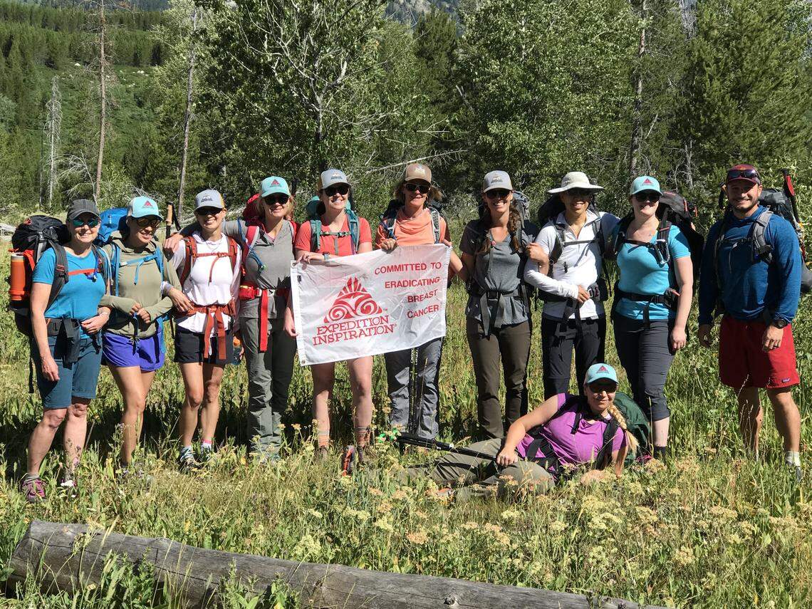 Eleven of the 12 people who climbed the Grand Teton with Expedition Inspiration pose together with a flag from the nonprofit, which raises funds for breast cancer research.