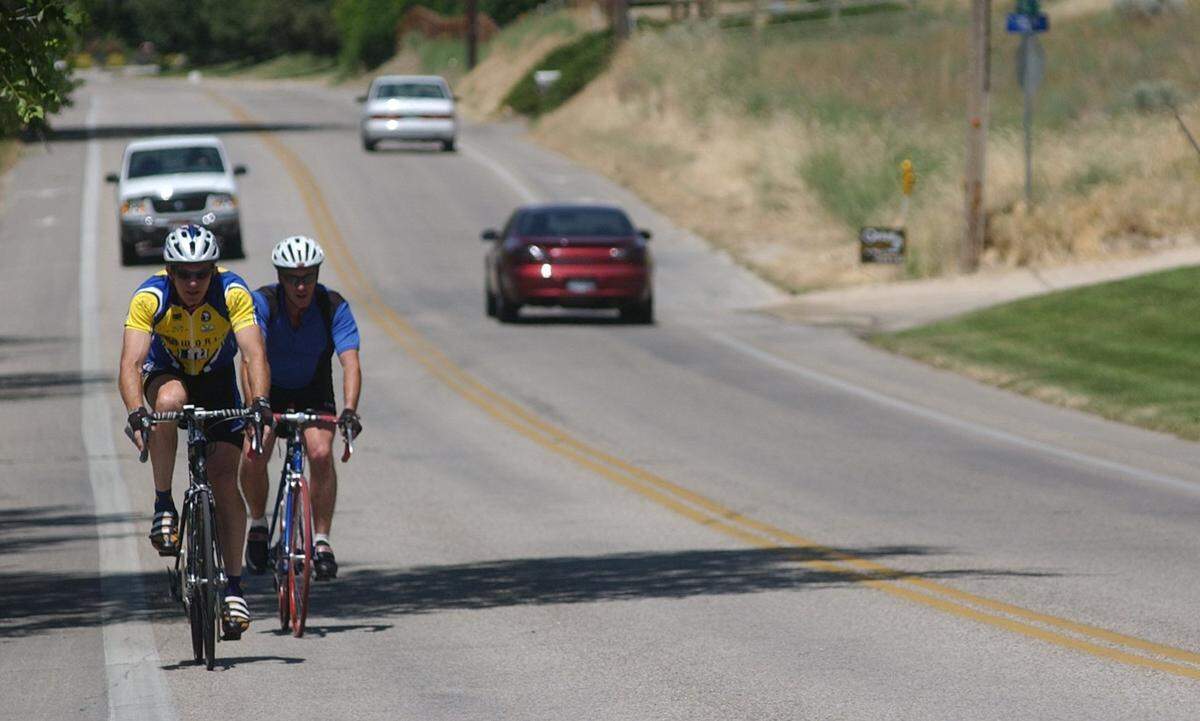 Cyclists pedal along Hill Road as motor vehicles pass in both directions.