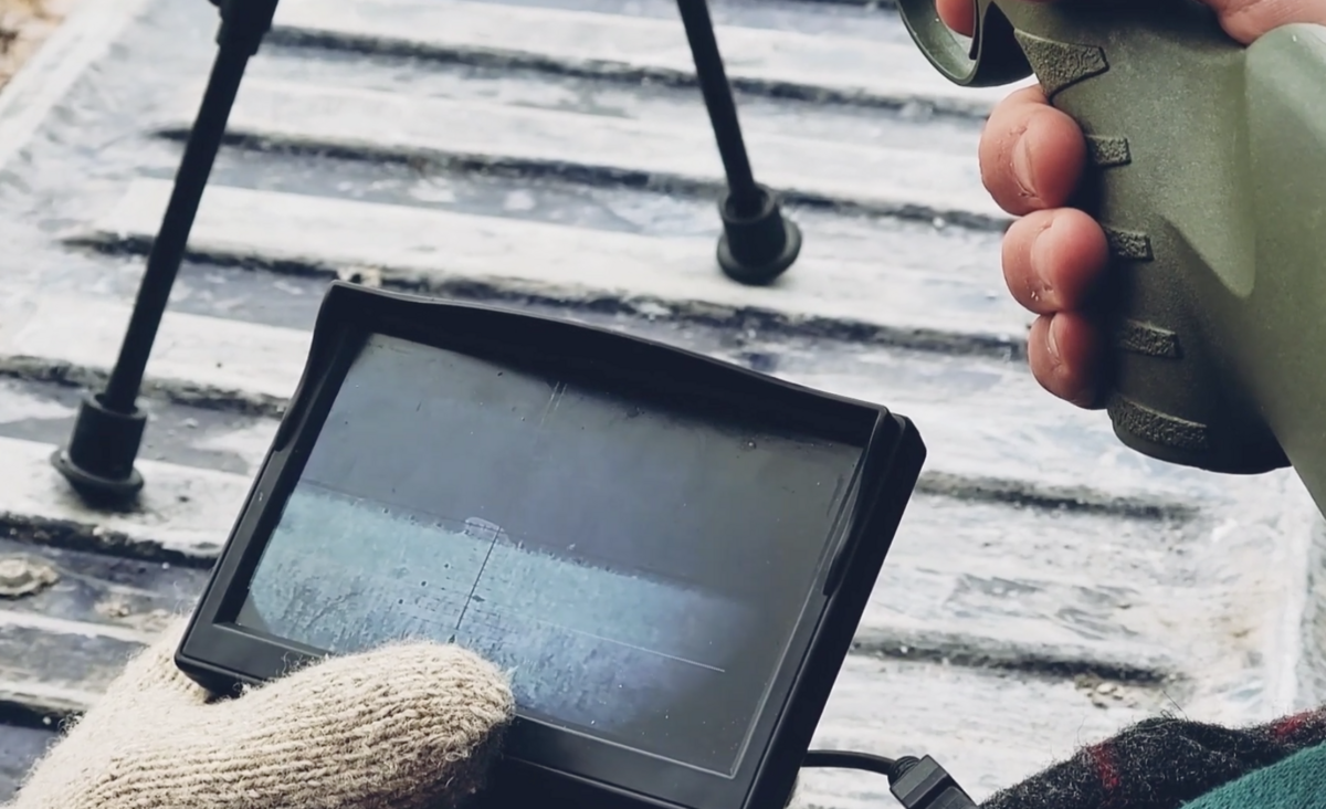 Caleb Linck holds an external scope camera displaying the image from his stepson Jade Harlow’s rifle sights. Harlow is blind, and Linck serves as his hunting companion, using the external display to guide Harlow to his target.