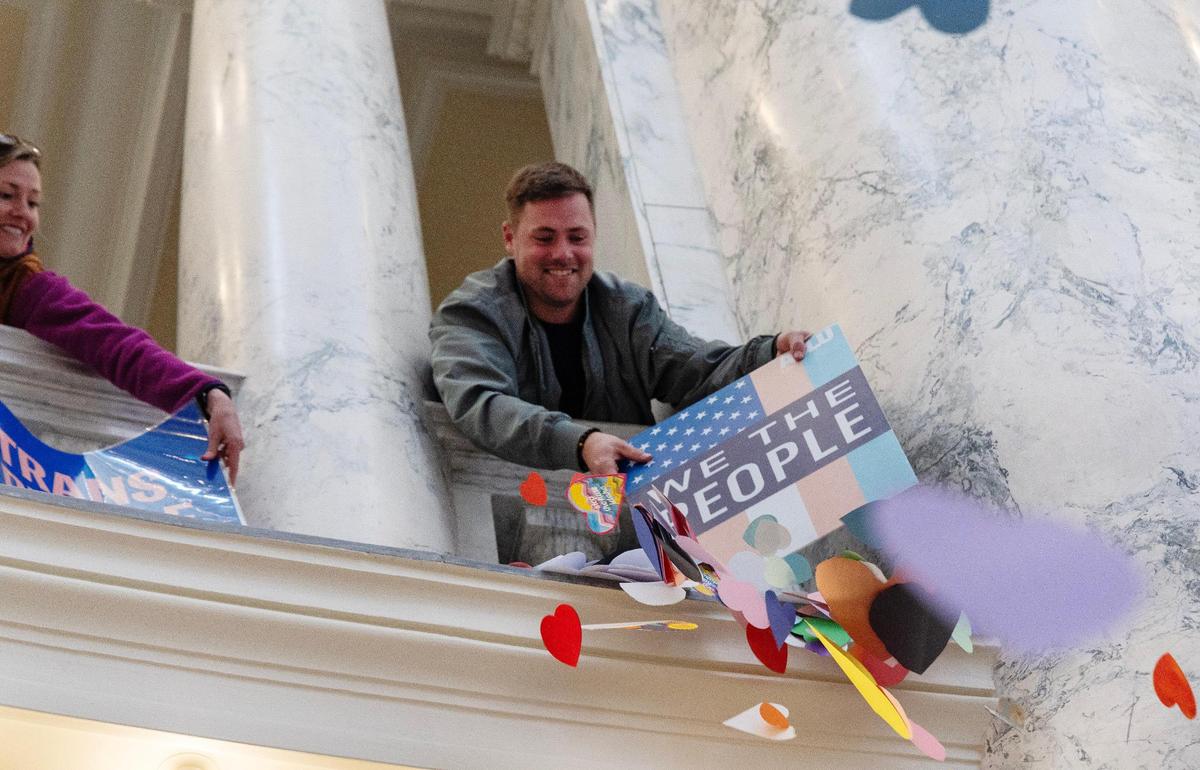 Logan Self of Boise uses a transgender rights sign to knock paper hearts off of a ledge of the Idaho Capitol rotunda during a demonstration, Tuesday, April 2, 2024.