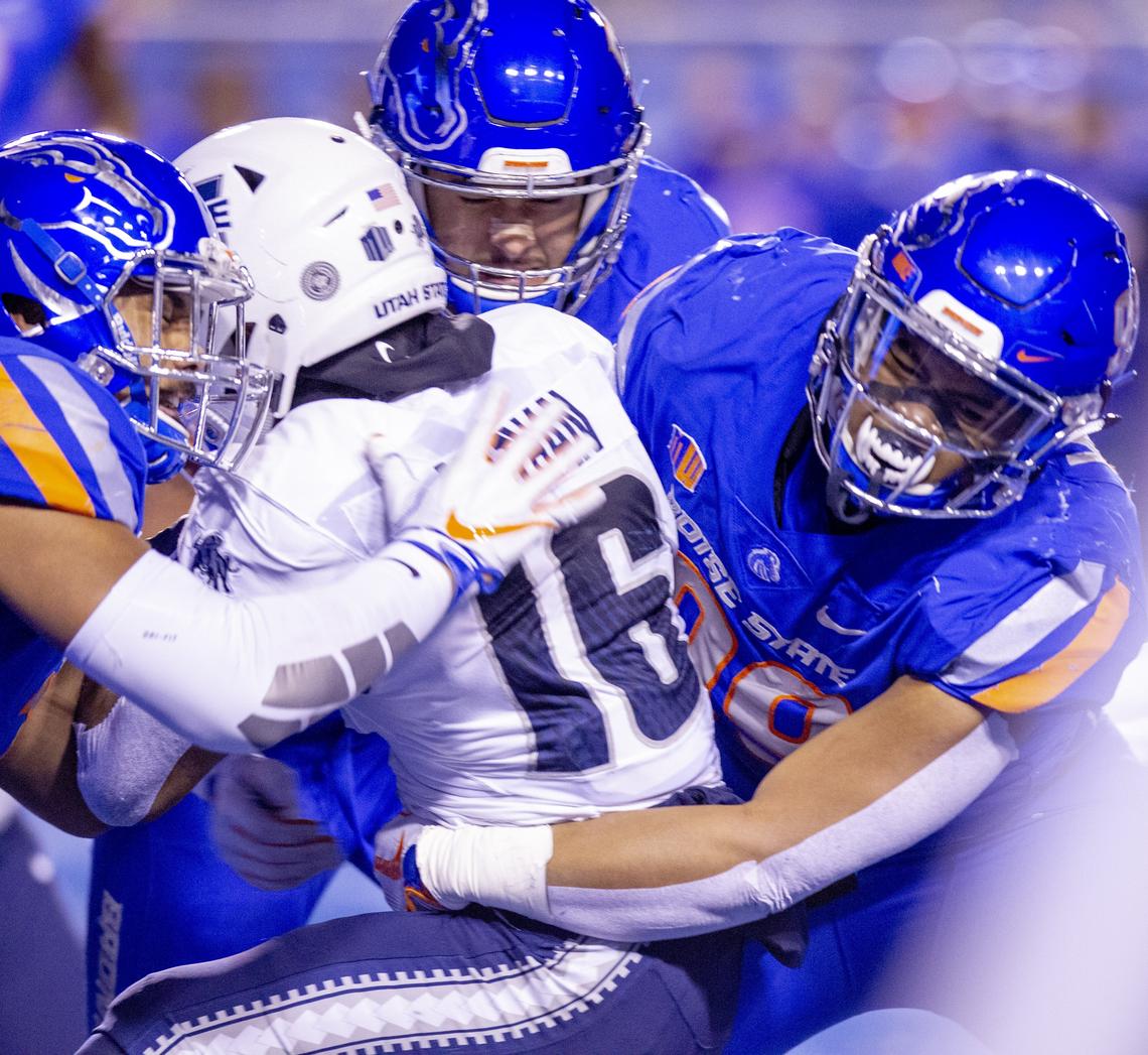 Boise State defenders Ezekiel Noa, left, and Curtis Weaver, right, combine to stop Utah State wide receiver Jordan Nathan.