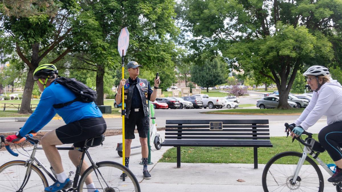 Mel Walker clocks the speed of bicyclists while holding a sign reading SLOW on the Greenbelt along Julia Davis Park.