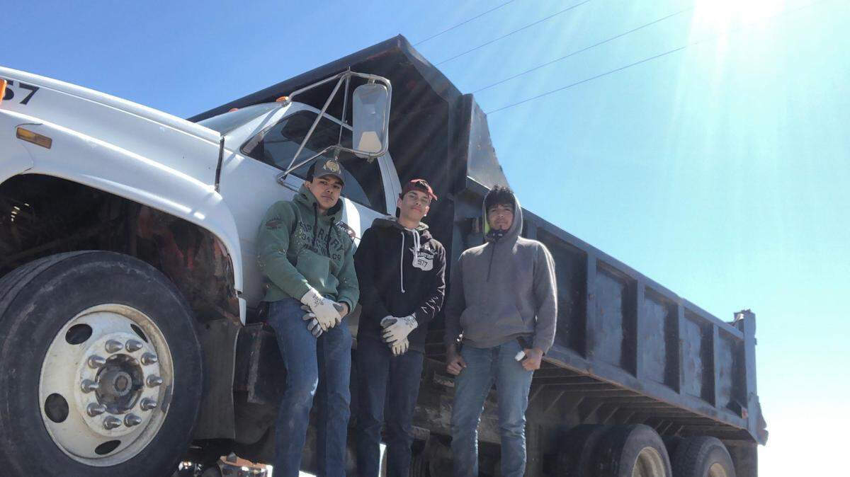 Los estudiantes de American Falls High School, Rafael Villa (izquierda), Edgar Soltero y Edwin Hernández posan para una foto frente a un camión de trabajo que usan para despejar los campos de piedras en el este de Idaho.