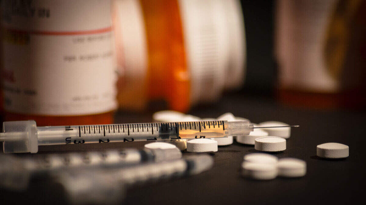 An injectable drug is loaded into a syringe while prescription medication is strewn about haphazardly.