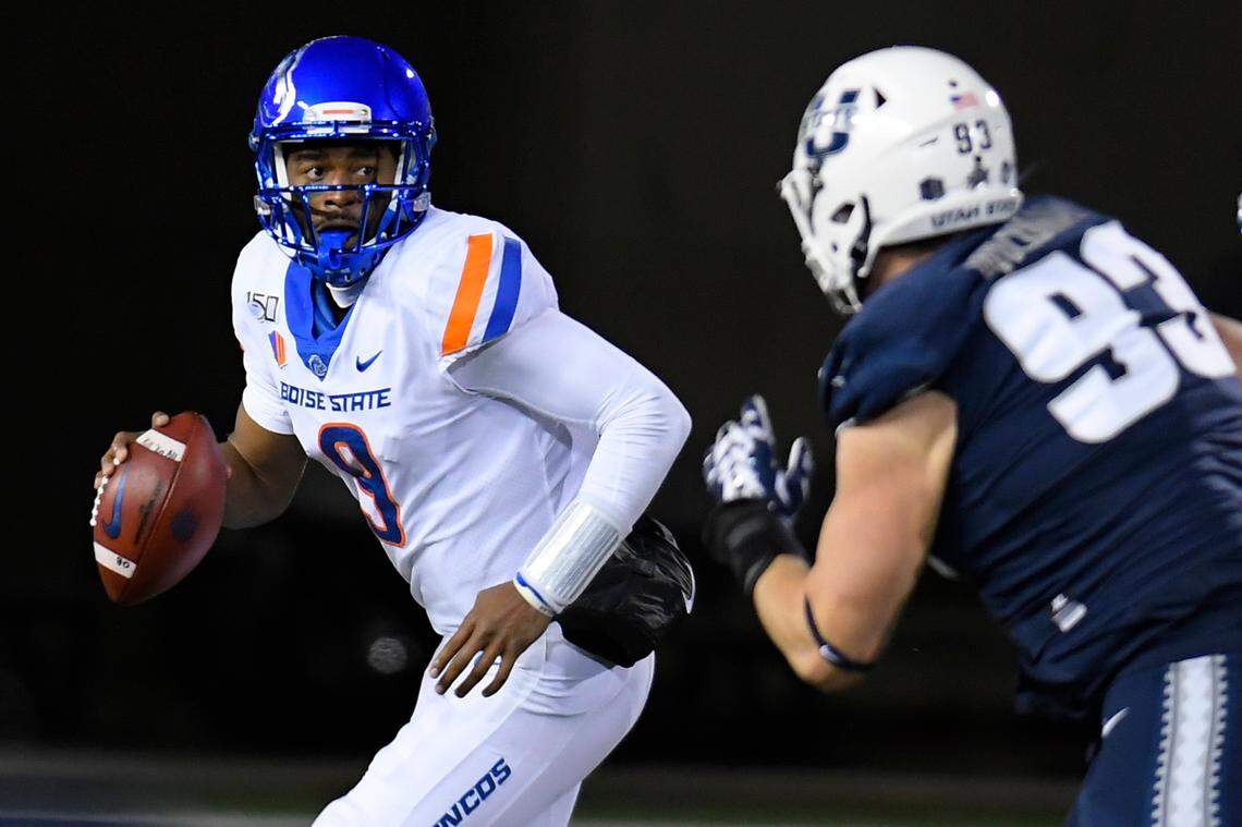 Boise State quarterback Jaylon Henderson looks for a receiver as Utah State defensive end Jacoby Wildman pursues during the first half Saturday in Logan, Utah.