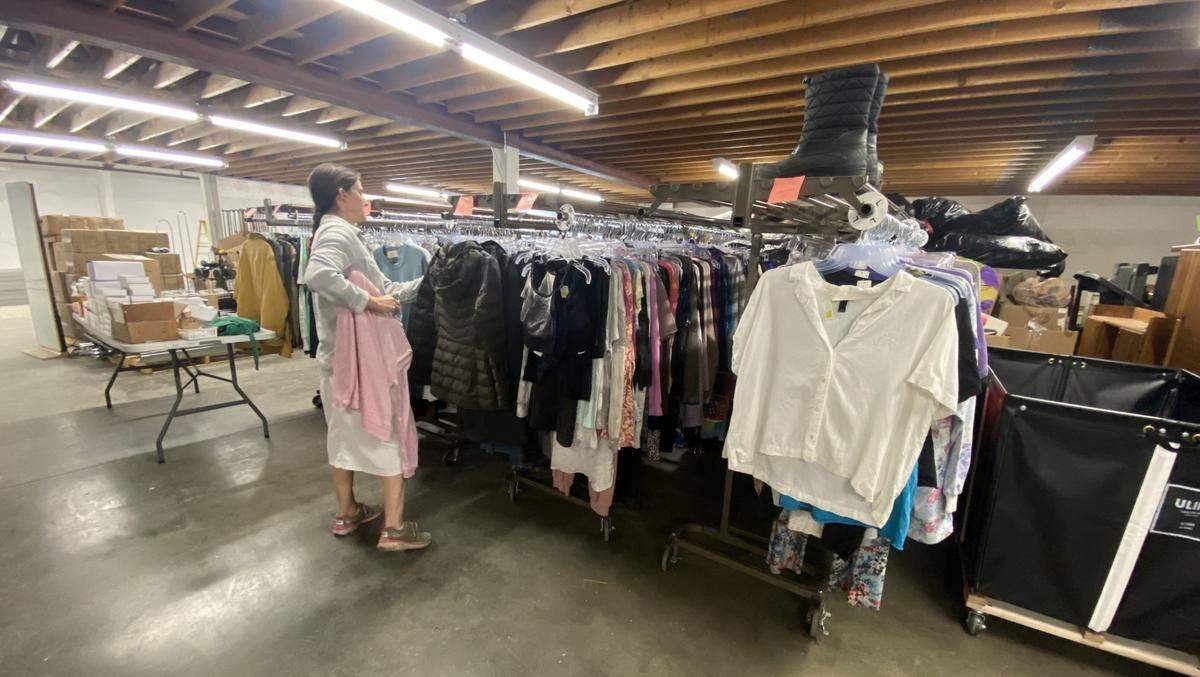 Lynn Weaver, co-manager at Impact Thrift, hangs donated clothes on racks inside the former Bench Commission building.